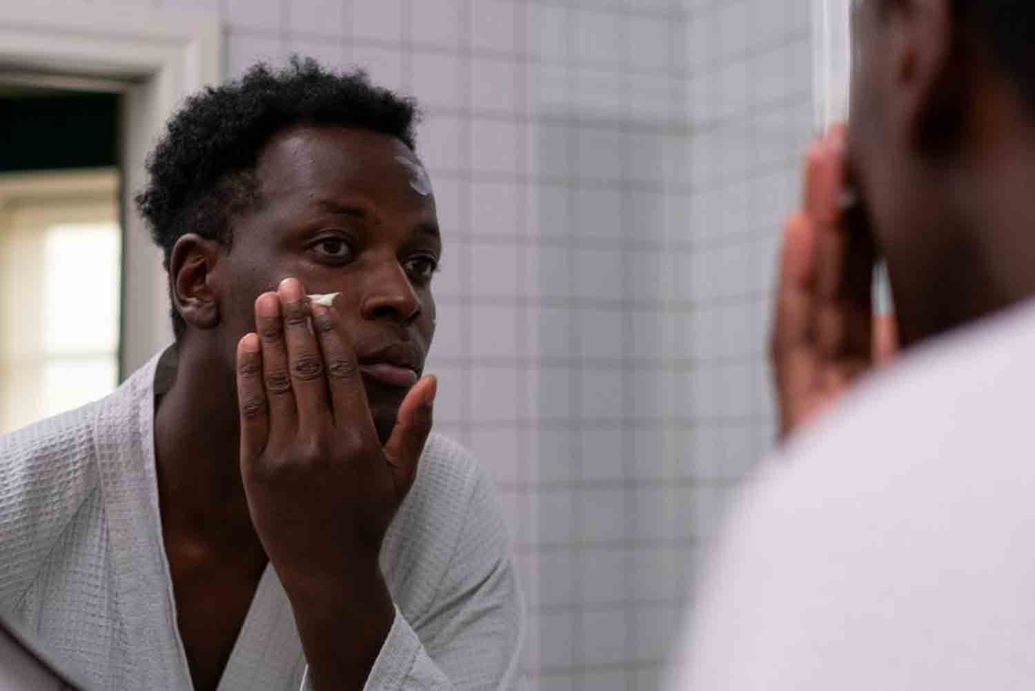 man applying moisturizer in mirror
