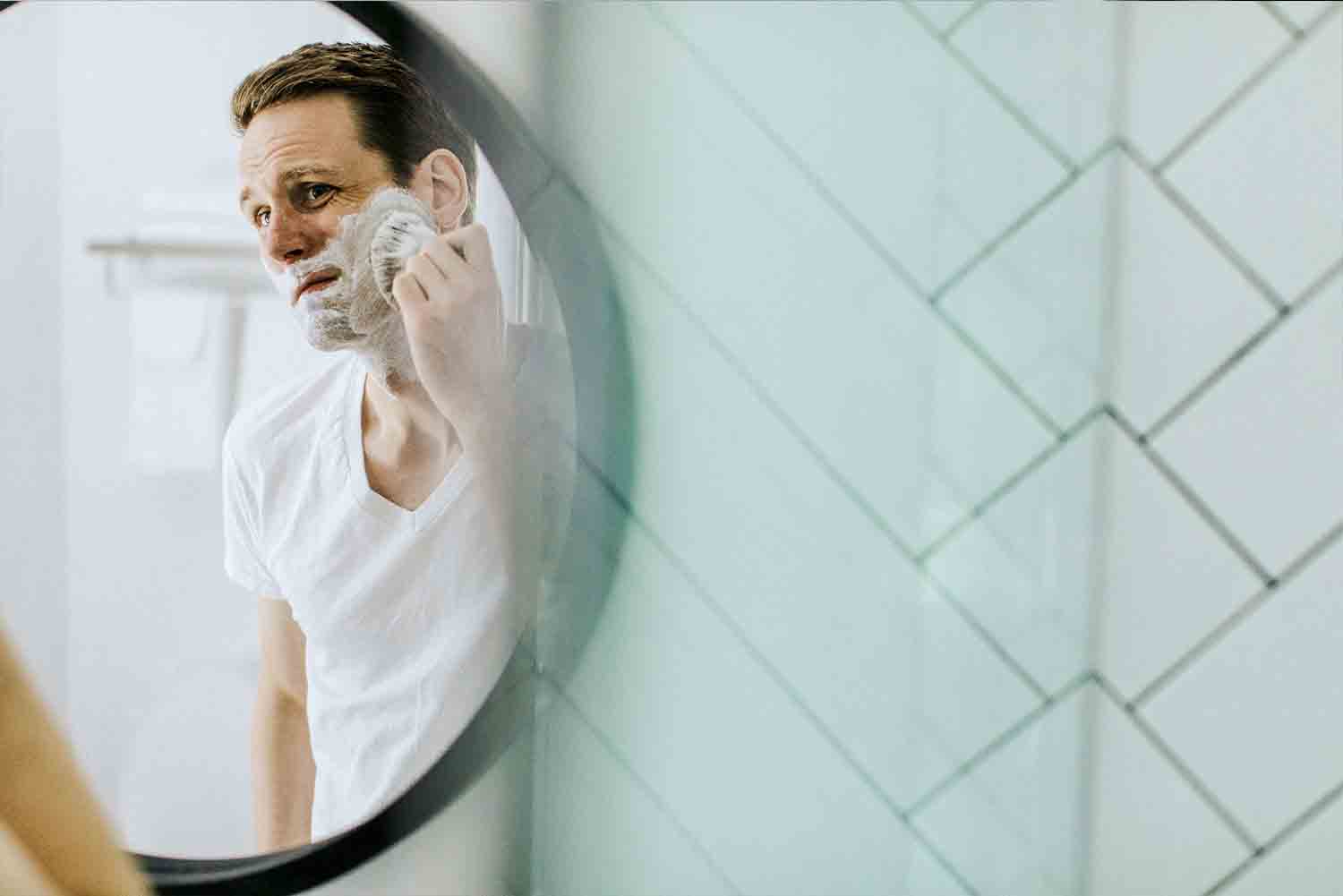 man applying shaving cream in bathroom mirror