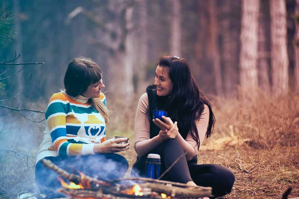 women camping by fire smiling conversing